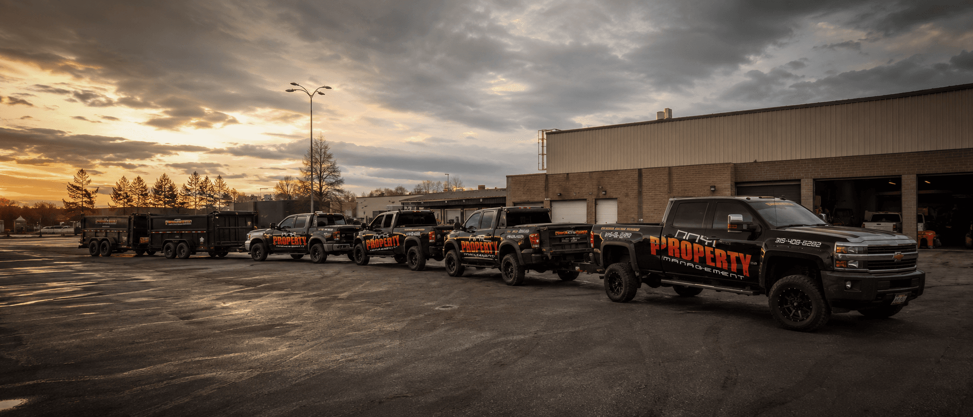 NNY Property Management fleet of trucks and dump trailers lined up at dusk